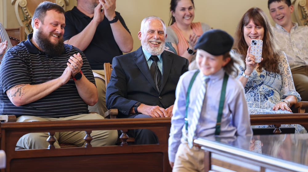 David Norman, center, laughs as his grandson Jackson Norman returns to his seat after speaking during a ceremony on Friday at the Miami County Courthouse in downtown Troy. David Norman was being honored for his service in the Marine Corps. He was one of the last Marines to be evacuated from the American Embassy during the fall of Saigon 50 years ago. David Norman's youngest son Nathan is seated to his left, and wife Susie is seated to his right. Jackson Norman is the son of Neal Norman, not pictured. BRYANT BILLING / STAFF
