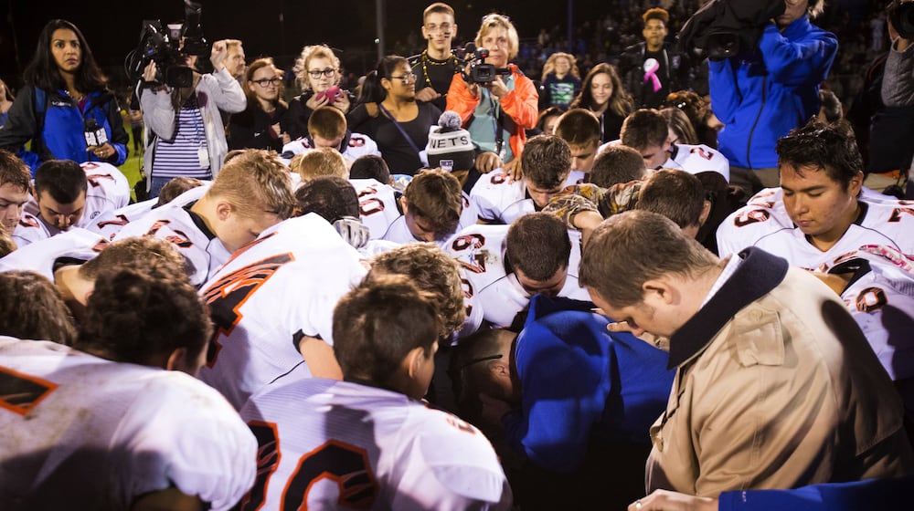 FILE - Bremerton High School assistant football coach Joe Kennedy, center in blue, kneels and prays after his team lost to Centralia in Bremerton, Wash., Oct. 16, 2015. Across America, most high school football seasons are winding down. It will wrap up the first year since the Supreme Court ruled it was OK for a public school coach near Seattle to pray on the field. (Lindsey Wasson/The Seattle Times via AP, File)